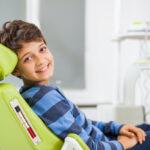 Brunette boy in a striped shirt smiles while sitting in a green dental chair at Safari Children's Dentistry & Braces in San Antonio, TX