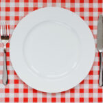 Empty plate setting with plate, knife and fork on red gingham background