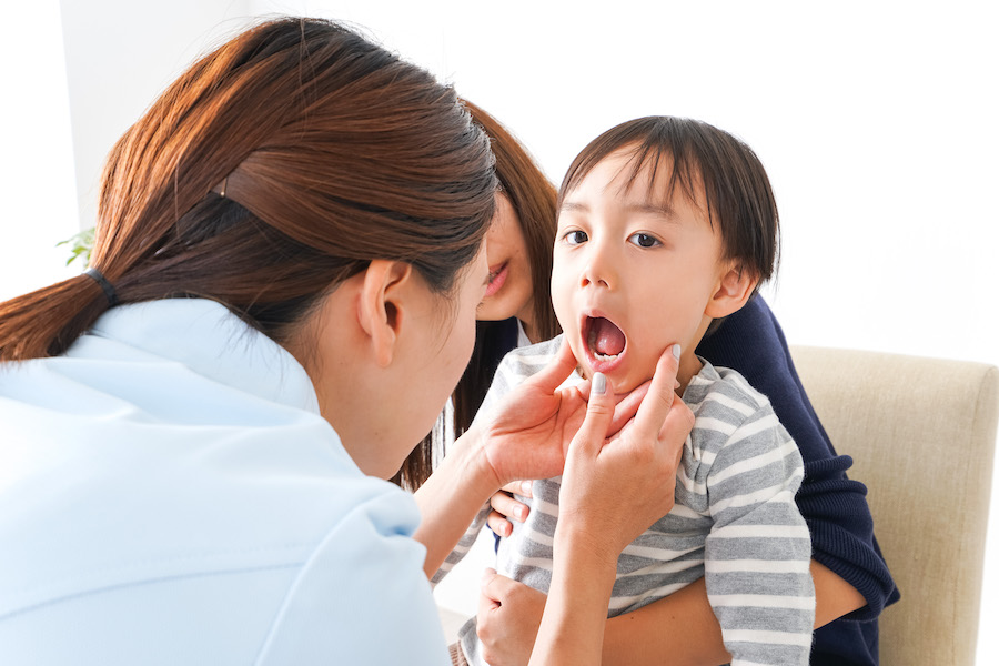 Brunette dentist looks into a child's mouth to see their crooked baby teeth as they say "ah"